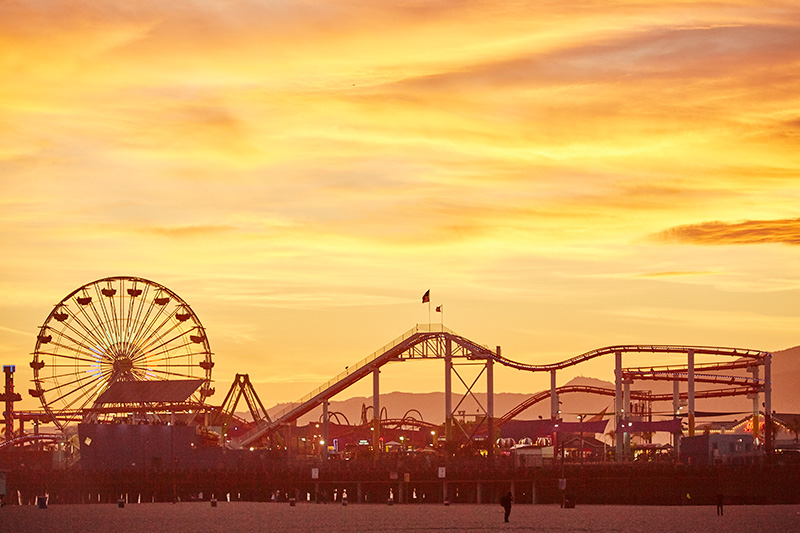 Santa Monica Pier sunset. Pacific Park, Ferris wheel, roller coaster, California coast.