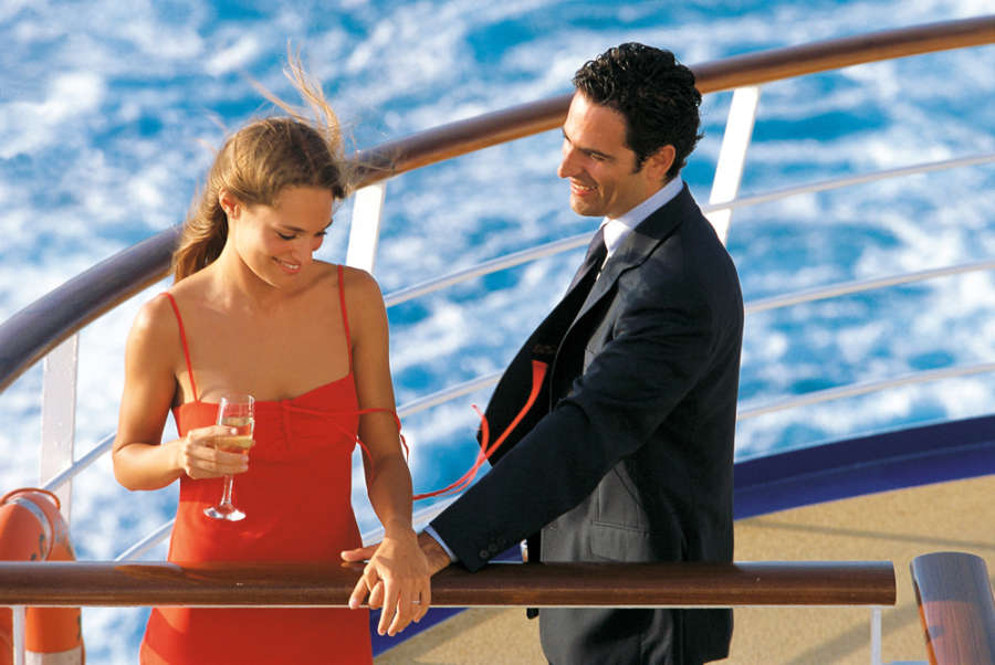 A happy couple enjoying a romantic moment on the deck of a cruise ship, with the ocean and sunset in the background.