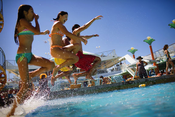 Guests jumping into the pool on a cruise ship, enjoying the sunny weather and fun atmosphere.