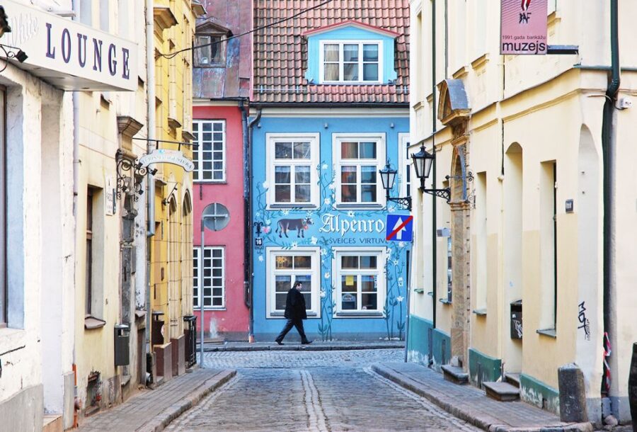 Vibrant street in Riga with colourful buildings, featuring a bright blue facade and a pink building. Cobbled street with a person walking in the distance.