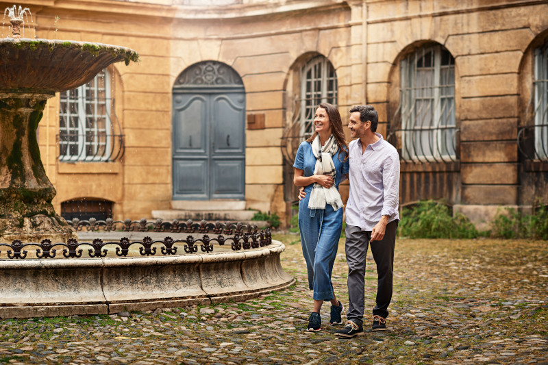 A picturesque view of a charming street in Aix-en-Provence, Marseilles, lined with colourful buildings and bustling with locals and tourists.