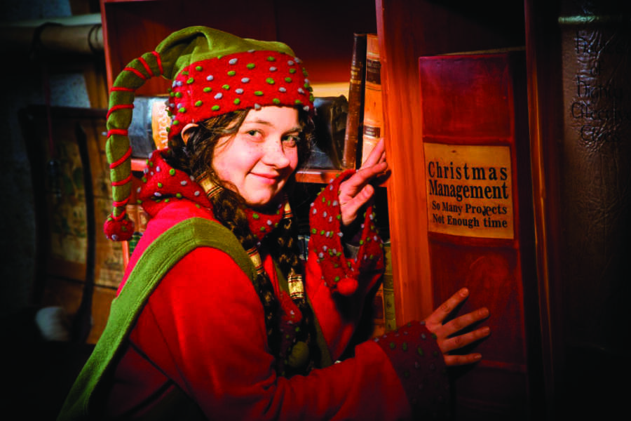 An elf smiling showing off Santa's workshop.