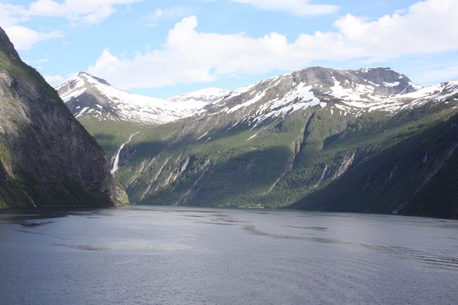 Majestic fjord scenery with snow-capped mountains, cascading waterfalls, and calm waters reflecting the sky. Experience Norway's natural beauty.