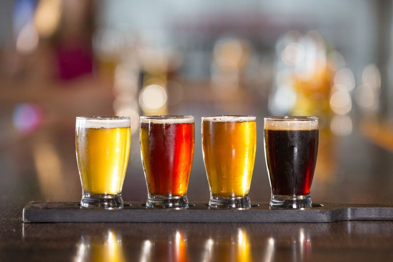 A flight of beer, showcasing a variety of different beer styles in small glasses. This image is often associated with beer tasting experiences and brewery tours, popular activities for travelers. Travel Escapes Cruises beer tasting, brewery tour, craft beer, flight of beer, beer variety