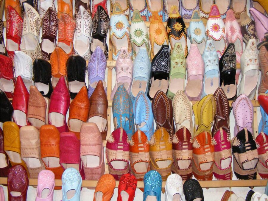 A bustling shoe market in Marrakesh, Morocco, with colourful stalls displaying a variety of shoes, and people exploring the market.