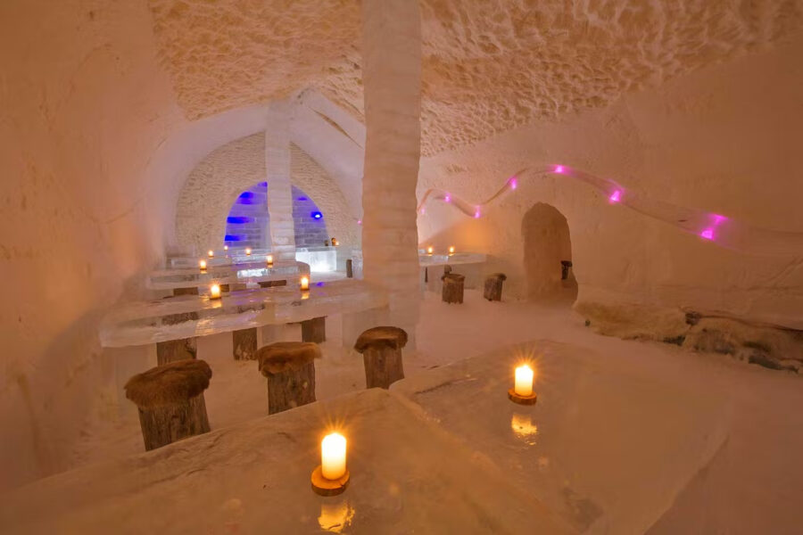 An interior of an igloo-style restaurant made entirely of ice, featuring ice tables and candles glowing warmly.