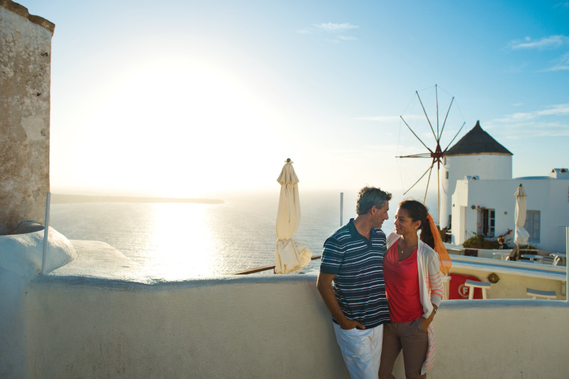 A couple sightseeing in Oia, Santorini, Greece, with white-washed buildings and blue domes in the background.