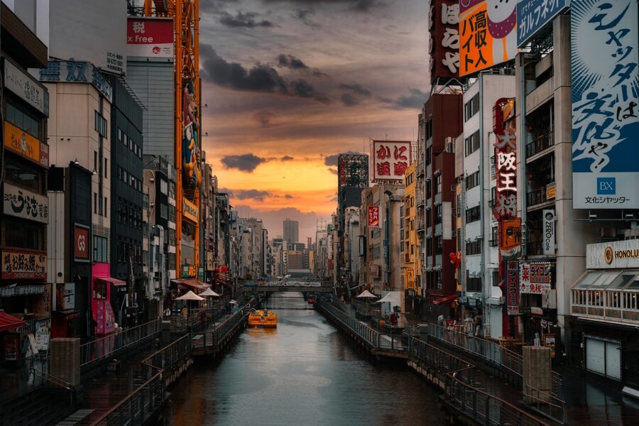 A scenic view of Osaka city with modern buildings lining the riverbanks and reflections shimmering on the water.