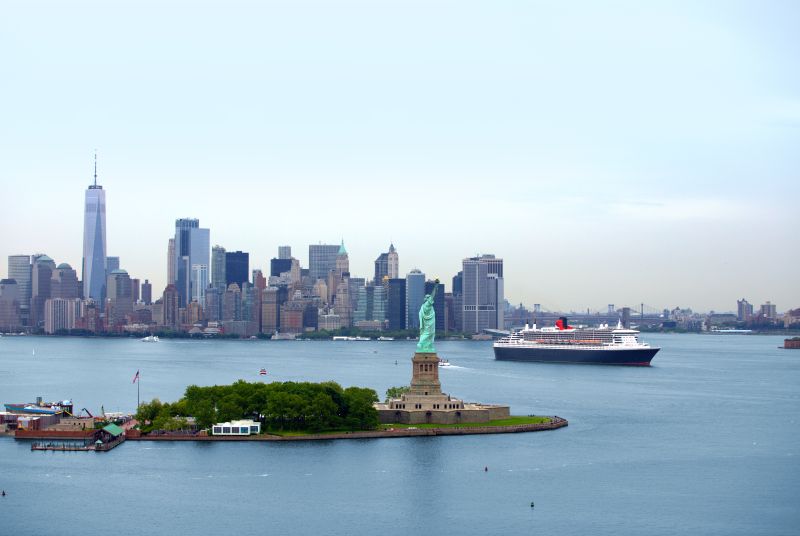  Panoramic view of the Statue of Liberty and the New York City skyline, with the Queen Mary 2 cruise ship passing by Ellis Island. Travel Escapes Cruises and Tours