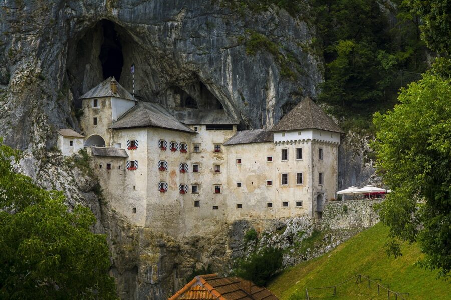 View of Predjama Castle built into the limestone cliffs at the entrance of a cave in Slovenia, creating a dramatic and unique medieval fortress. Surrounded by lush greenery, this iconic attraction near the Postojna Cave is a remarkable blend of natural and architectural beauty