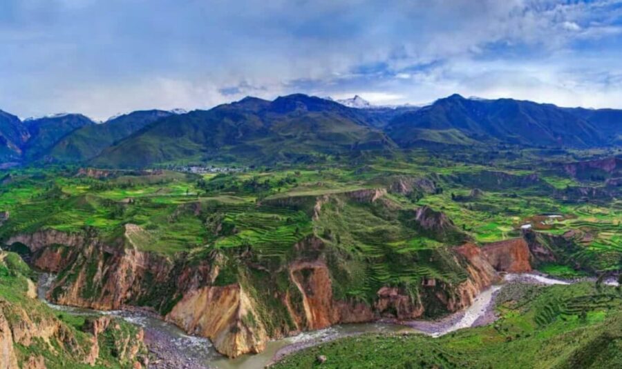 Colca Canyon, Peru. Deep canyon with river, patchwork fields on slopes, mountains in distance, dramatic sky.