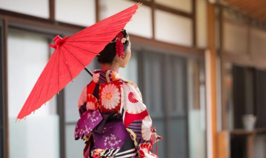Woman in colourful kimono, red umbrella. Traditional Japanese attire, walking outdoors, blurred background.