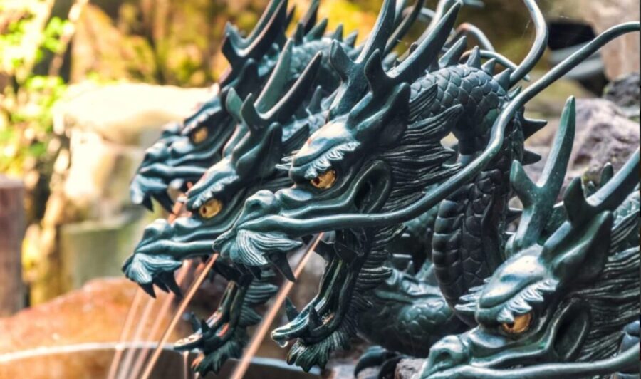 Three ornate dragon head sculptures, dark metal, detailed scales and piercing eyes, blurred background. Japan.