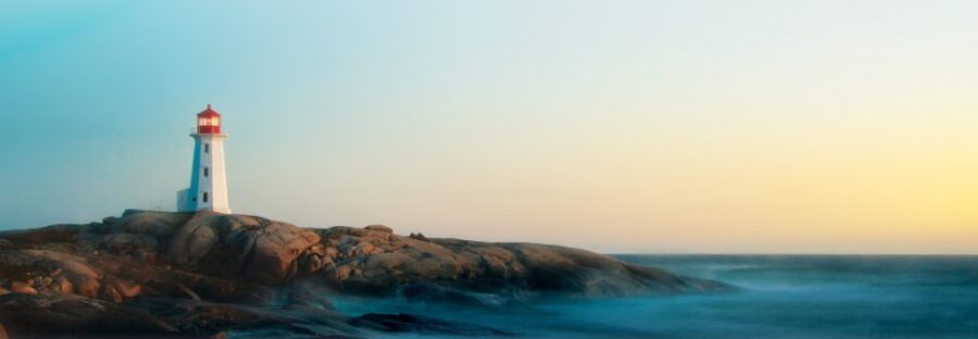 Waves gently crash against rugged coastal rocks beneath a pastel sky at sunset, creating a serene and scenic seascape.