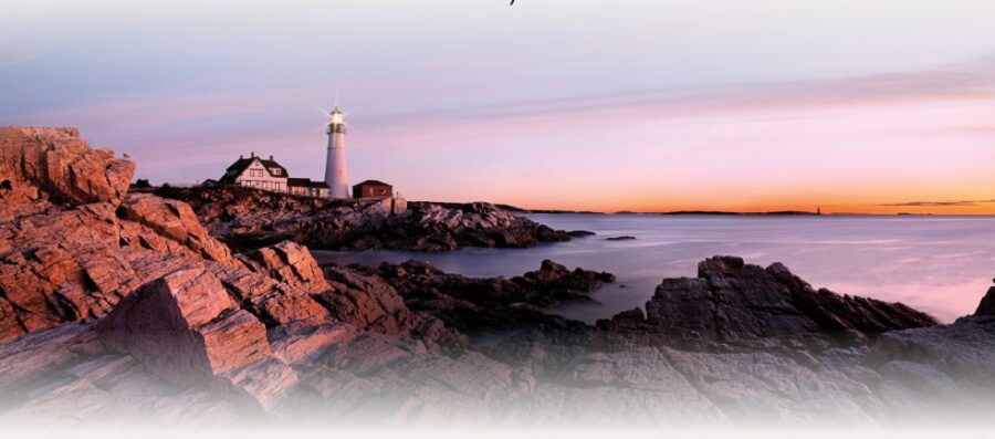 A lighthouse stands on a rocky coastline at sunset, casting light over calm waters under a pastel-hued sky.