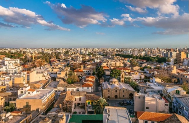 Aerial view of Nicosia, Cyprus, showing a mix of modern and traditional architecture under a blue sky with scattered clouds.