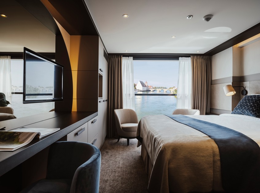 Travelmarvel cabin interior with bed, seating, and river view through large window. Comfortable and modern river cruise accommodation.