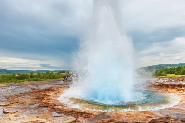 Witness the raw power of nature as Iceland's Strokkur geyser erupts, sending a towering jet of boiling water high into the air. This incredible natural spectacle, set against a backdrop of geothermal landscape and cloudy skies, is a thrilling reminder of Iceland's volcanic activity. A truly unforgettable sight and sound!