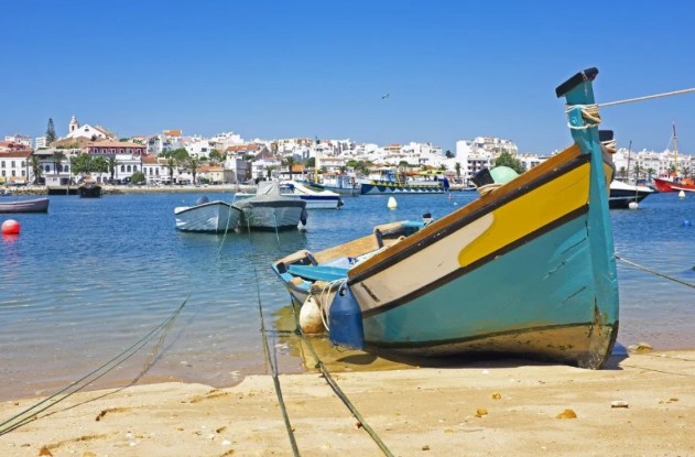 Colourful fishing boat in Lagos harbour, Portugal. Bright blue hull with yellow trim. Town visible in the background across the water. Sunny day, clear blue sky.