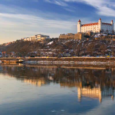 Majestic Bratislava Castle perched high above the Danube River, beautifully reflected in the calm waters on a clear winter's day.