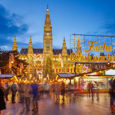 Vienna's magnificent Rathaus illuminated at night, towering over the bustling Christkindlmarkt with its twinkling lights and festive
