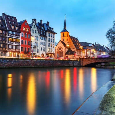 Enchanting Rhine riverside city at dusk, colourful historic buildings and illuminated church reflecting in the water, perfect for festive river cruises.