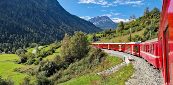 The iconic Bernina Express train travelling through the magnificent alpine scenery of the Dolomites and Swiss Alps on a clear day.