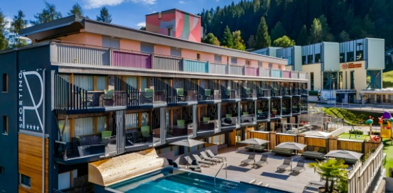 The Sporting Hotel in the Italian Dolomites, featuring a modern design, outdoor swimming pool with loungers, and balconies with mountain views.