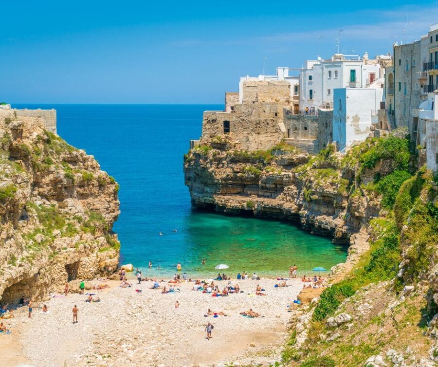 The iconic cove beach of Lama Monachile in Polignano a Mare, Puglia, nestled between dramatic cliffs with sunbathers on the pebbles.