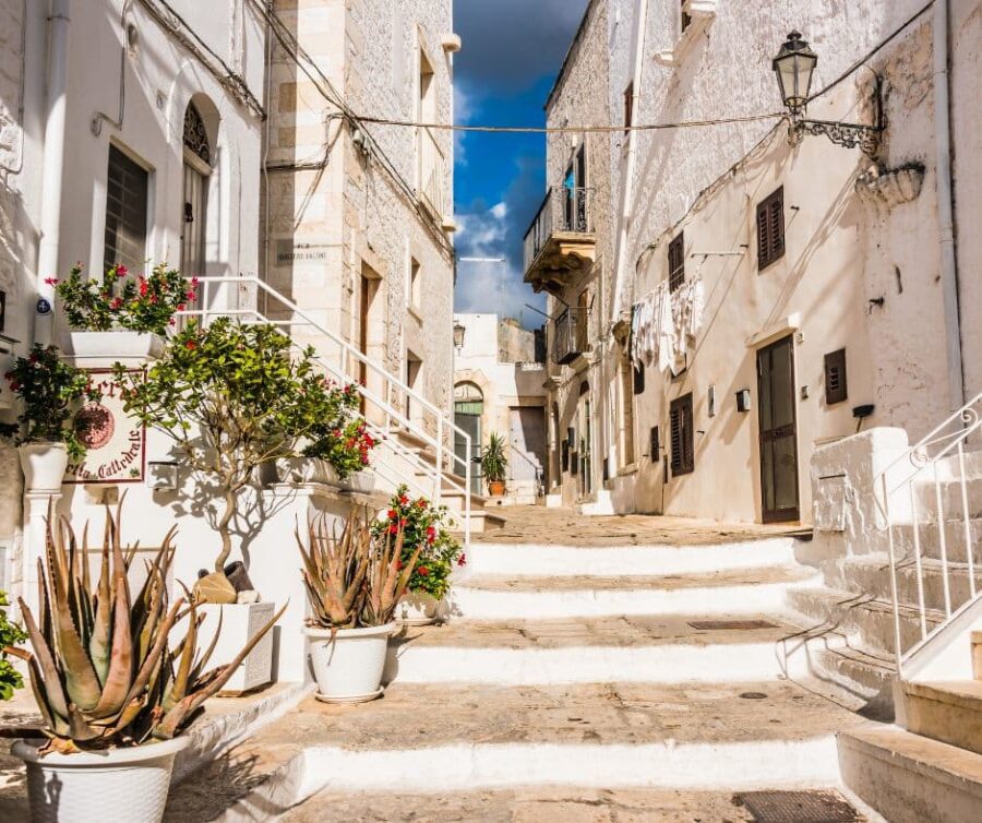 Steps leading up a narrow alleyway between whitewashed buildings with potted plants in the historic centre of Ostuni, Puglia, Italy.